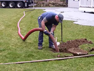 Septic pumping technician servicing a residential septic tank with a vacuum hose in Burlington, VT