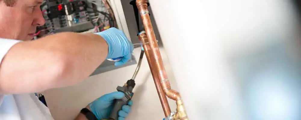 Water heater repair technician testing copper pipe connections and controls in Burlington, VT